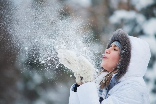 Девушка дует снег с ладошек